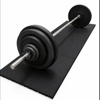 A barbell with black weight plates resting on a black rubber gym mat